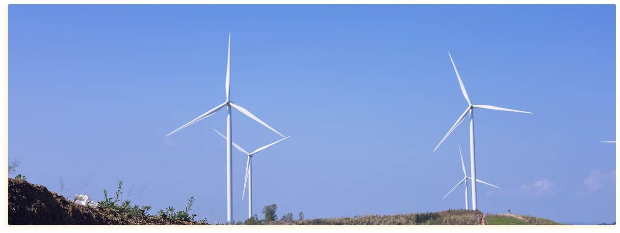 Drie windturbines staan op een met gras begroeide heuvel onder een strakblauwe hemel. Het tafereel straalt een gevoel van rust en duurzame energie uit.