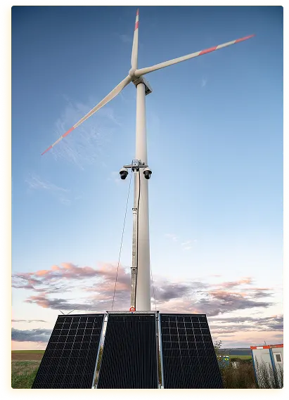 Een hoge windturbine naast zonnepanelen staat tegen een helderblauwe lucht bij zonsondergang. Het tafereel straalt een gevoel van duurzame energie en rust uit.